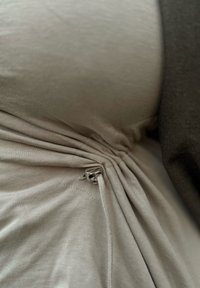 Lichtbeige, geplooide stof met een zichtbaar zilveren metalen accent en trekkoorddetail. Textuurrijke katoenmix met een gladde afwerking.