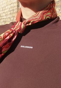 Barna ing fehér "SALOMON" logóval; színes, mintás sállal díszítve, amely piros, rózsaszín és zöld hullámokat tartalmaz.