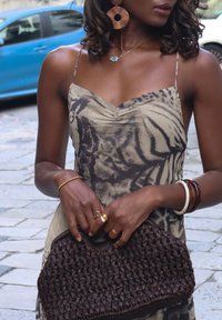 Lendlev kleit loomamustriga, beeži ja tumedat halli värvi. Spagetirihmad, kogutud kaelus. Käes on kootud tumepruun käekott tekstuurse detailiga.