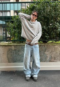 Pull court gris clair avec un col polo, associé à un jean denim bleu clair surdimensionné. Chaussures noires aux semelles texturées et ceinture marron.