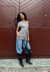 Sivi, teksturirani top s jednim rukavom s točkicama, uparen s širokim, izblijedjelim plavim trapericama i crnim čizmama do koljena. Crna prošivena torbica.