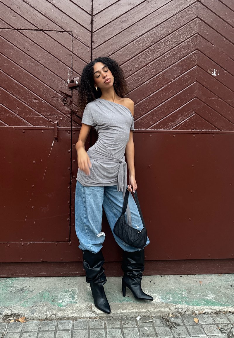 Pilkas, tekstūruotas, viena petneša palaidinė su polka taškais, derinama su laisvais, išblukusiais mėlynais džinsais ir juodais aulinukais iki kelių. Juoda siuvinėta rankinė.