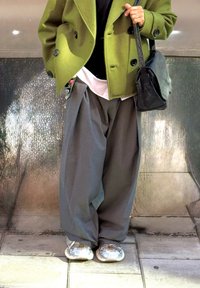 Groene dubbele wollen jas, zwarte top, grijze wijde broek, zilveren sneakers en een kleine zwarte leren tas.