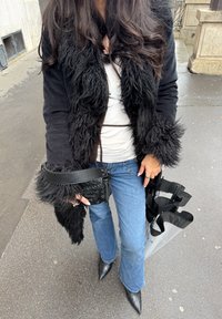 Mustast sasipunutisest kunstkarvast mantel valge topi kohal, ühes välja lõigatud teksade ja mustade teravate varvastega saapadega. Kuulub väikese musta käekoti ja detailidega komplekti.