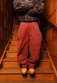 Άτομο που στέκεται σε ξύλινη σκάλα, φορά καφέ φλις μπουφάν, κόκκινο καρό παντελόνι με αλυσίδα και ταμπά μπότες.