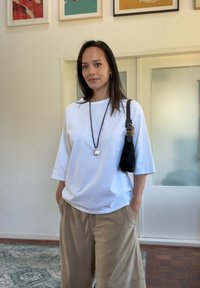 Biała bawełniana, oversize'owa koszulka z trzema ćwiartkami rękawów, połączona z khaki szerokimi spodniami. Czarna torebka na ramię z plecionym paskiem i srebrnym wisiorkiem.