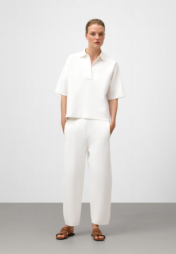 Weißes, locker sitzendes Kurzarmoberteil mit Kragen, kombiniert mit passenden weißen Hosen und braunen Sandalen. Weiche Textur, modernes Design.
