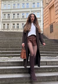 Brauner langer Mantel, weißer Zopfpullover, braune Lederhosen, dunkle Strumpfhosen, kniehohe braune Stiefel und eine braune Handtasche, die steinerne Stufen hinabsteigend.