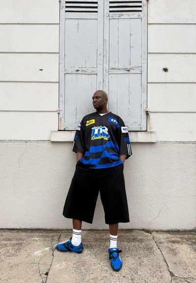 Conjunto deportivo en negro y azul que incluye una camiseta de manga corta con rayas, pantalones cortos negros de corte amplio y calzado azul con detalles en negro.