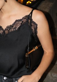 Top de cetim preto com rendas, combinado com uma pequena bolsa preta com fecho e alça dourados. Tecido texturizado e design elegante.