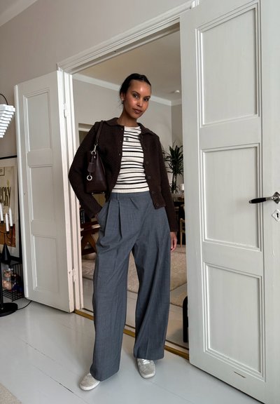 Cárdigan marrón texturizado, camisa a rayas, pantalones de pierna ancha grises y zapatillas plateadas, con un bolso que tiene un acento circular.