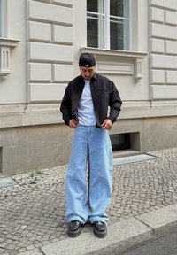 Fekete gombos ing fehér póló fölött, világoskék bő szárú farmerrel és fekete platform cipővel, világos fal előtt.