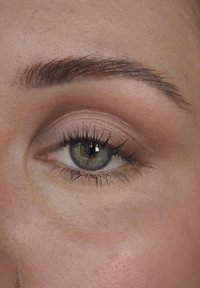 Close-up van een groen oog met lange, donkere wimpers en subtiele oogschaduw. De huid rondom het oog is glad, met een lichte textuur en natuurlijke tinten.