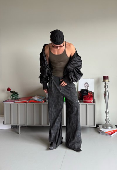 Chaqueta bomber acolchada negra, top de tanque oliva y pantalones anchos negros con patrón. Unidad de almacenamiento gris con revistas y una vela al fondo.