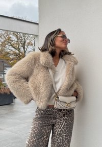 Faux fur cropped jacket in beige, featuring a plush texture and wide collar. Paired with leopard-print trousers and a small cream bag with gold hardware.