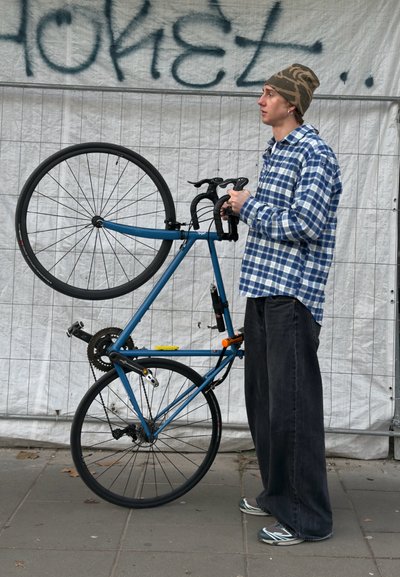 Bicicleta azul mantenida en posición vertical con una rueda levantada del suelo; cuenta con manillares tipo gota, neumáticos negros y un diseño de cuadro minimalista.