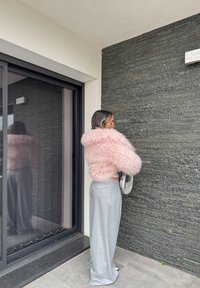 Pink fuzzy jumper with a hood, paired with light grey wide-leg trousers. Smooth texture and a reflective silver bag complete the outfit.