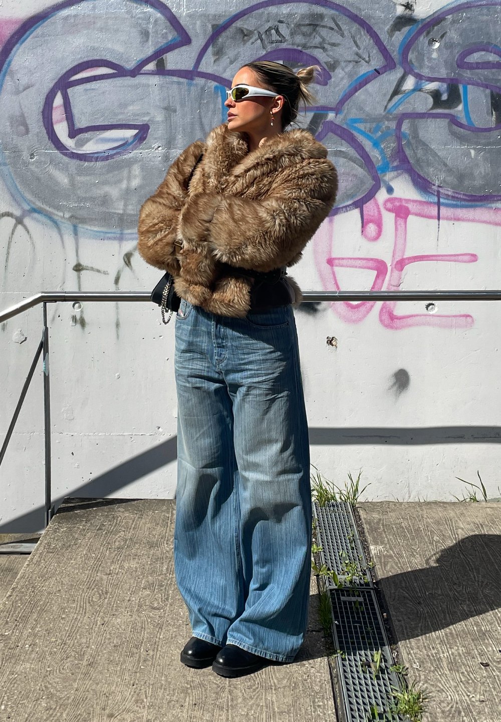 Faux fur brun jakke med en bred krave, parret med lyseblå oversized jeans. Sorte platform sko og hvide solbriller fuldender looket.