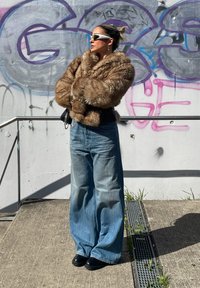 Faux fur brun jakke med en bred krave, parret med lyseblå oversized jeans. Sorte platform sko og hvide solbriller fuldender looket.