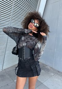 Maglia nera a maniche lunghe in rete con un motivo testurizzato, indossata sotto una cintura corsetto nera. Abbinata a una minigonna in denim nera con tasche.