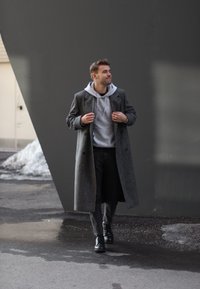 Szary wełniany płaszcz, szara bluza z kapturem, czarne dżinsy i czarne skórzane buty. Płaszcz ma podwójnie zapinany krój z dużymi guzikami.