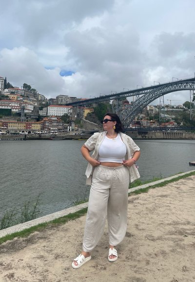 Conjunto de lino de color beige claro con una parte superior blanca corta y pantalones holgados, combinado con sandalias blancas y gafas de sol negras de gran tamaño.