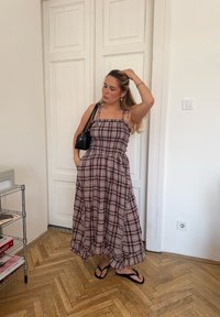 Maxikjole med brunt og hvitt rutemønster, justerbare stropper, samlet midje, swung Skirt, kombinert med svarte flip-flops og en liten svart veske.