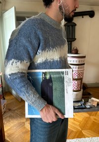 Pull texturé gris et bleu avec un col rond ; tenant une pochette d'album carrée présentant une image de véhicule et des bords usés.