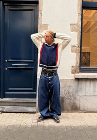 Pletený sveter na gombíky v krémovej a námorníckej modrej farbe s červenými akcentmi, doplnený o široké tmavomodré džínsové nohavice. Voľný strih s veľkými gombíkmi a opaskom s logom.