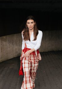 Bela majica s dolgimi rokavi, rdeč pas kot akcent in rdeča dodatna oprema; rdeče in bele kariraste široke hlače z teksturiranim zaključkom. Položaj pri hoji.