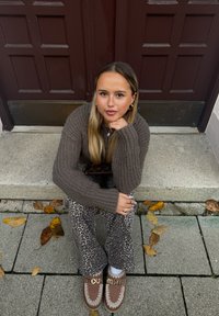 Καφέ πλεκτό πουλόβερ, παντελόνι με animal print και καφέ loafers με διακοσμητικά στοιχεία. Καθισμένος σε σκυρόδεμα σκαλοπάτια, με διασκορπισμένα φθινοπωρινά φύλλα.