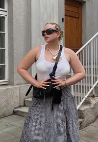 Svart crossbody-väska, vit tanktop, lager av pärl- och hjärt-halsband, svart-vitt rutigt kjol, stora solglasögon, långa naglar med mönster.