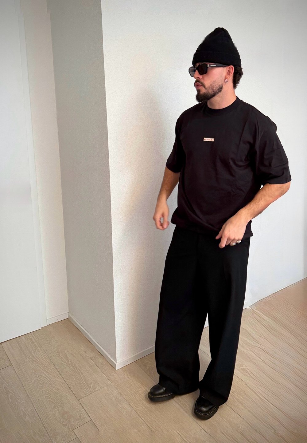 Fekete túlságosan nagy méretű póló kis logóval, széles fekete nadrágok, fekete sapka, napszemüveg és sötét cipők; sima szövet és laza szabás.