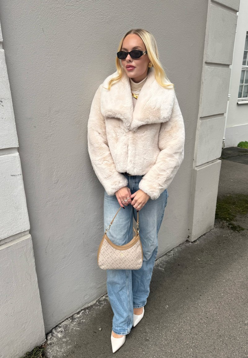 Cremefarbige Jacke aus Kunstpelz, helle Jeans aus Denim, weiße spitze High Heels und eine beige gemusterte Handtasche. Accessoires umfassen schwarze Sonnenbrillen. Glatte Texturen.