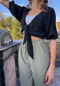 Black cropped blouse with tie-front, short puff sleeves; paired with light green pleated trousers featuring an elastic waistband.