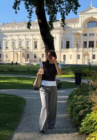 Ležerna odjeća koja se sastoji od tamnog bezrukavnog topa preko bijele košulje, sivi široki hlače, drži šalicu, uz uzorčastu torbu.