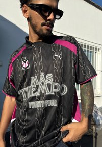 Zwart short-sleeve voetbalshirt met roze accenten, voorzien van een gestructureerd bladenpatroon, "Más Tiempo" graphic en Puma-logo.