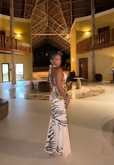 Mujer con vestido sin espalda con estampado de cebra y sandalias de pie en una habitación espaciosa, iluminada cálidamente, con techo alto de madera y suelo con patrón circular.