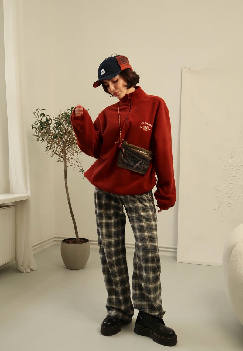 Κόκκινο φleece pullover με φερμουάρ μέχρι το μισό, καρό παντελόνι με φαρδιά πόδια, μαύρες πλατφόρμες μποτάκια και καπέλο με πολλές αποχρώσεις. Μικρή τσάντα ώμου με σχεδίαση από πλέγμα.