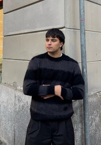 Maglione a righe nere e grigie realizzato in un materiale morbido e peloso. Presenta una scollatura tonda e polsini a coste; abbinato a pantaloni neri ampi.