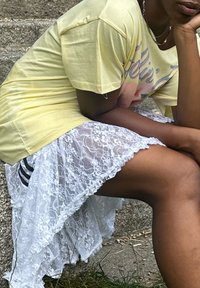 Gul t-shirt med grafisk print, lagdelt over en gennemsigtig hvid laceskirt med flæset kant. Udfordret ben synligt.