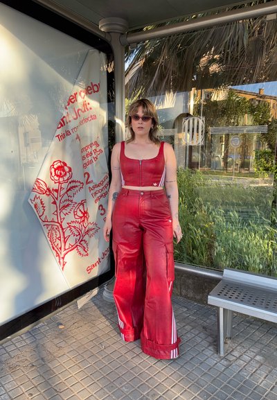 Top corto de cuero sintético rojo con cierre de cremallera, combinado con pantalones amplios de cuero sintético rojo que presentan franjas blancas y bolsillos tipo cargo.