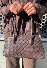 Hnedá tkaná leather taška s dvoma zaoblenými držadlami a štruktúrovaným tvarom. Obsahuje uzavretie na zips a hladký, lesklý povrch.