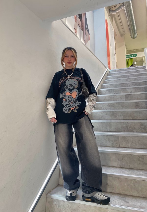 Sort oversized T-shirt med dødningehoved grafik, hvide lange ærmer. Løse grå jeans, sort og hvid sneakers, sølv kædehalskæde, sort taske.