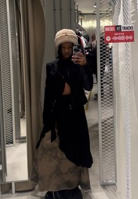 Μαύρο κοντό σακάκι, καφέ φούστα με νεροχύτη και φούντες στην άκρη, και ένα καφέ χνουδωτό καπέλο. Ανακλαστικός καθρέπτης σε εμπορικό περιβάλλον.