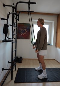 Młody mężczyzna używający gum oporowych przymocowanych do ściennego sprzętu fitness w jasnym pomieszczeniu do ćwiczeń w domu.