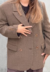 Blazer oversize marrone con motivo a spina di pesce, doppio petto, grandi bottoni e rever a lancia; il tessuto ha una finitura testurizzata.