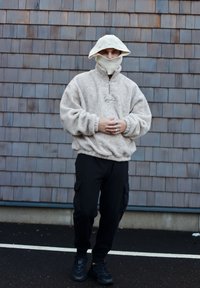 Pull-over en polaire beige avec col demi-fermeture éclair, associé à un pantalon cargo noir et des baskets noires ; portant un chapeau en tricot à large bord.