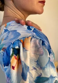 Μπλούζα με λουλουδάτο τύπωμα, φτιαγμένη από μαλακό, σιελινό ύφασμα σε �αποχρώσεις του μπλε και του πορτοκαλί, με φουσκωτά μανίκια και λεπτομέρειες ραψίματος.