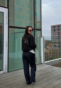 Jachetă oversized neagră, top alb și pantaloni negri cu picioare largi. Accesoriile includ o geantă mică neagră și ochelari de soare. Clădire în fundal.
